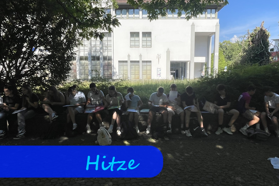 Vor Büschen auf Sitzbänken sitzen Jugendliche mit Büchern und Heften auf den Knien. Der Platz ist sehr schattig.